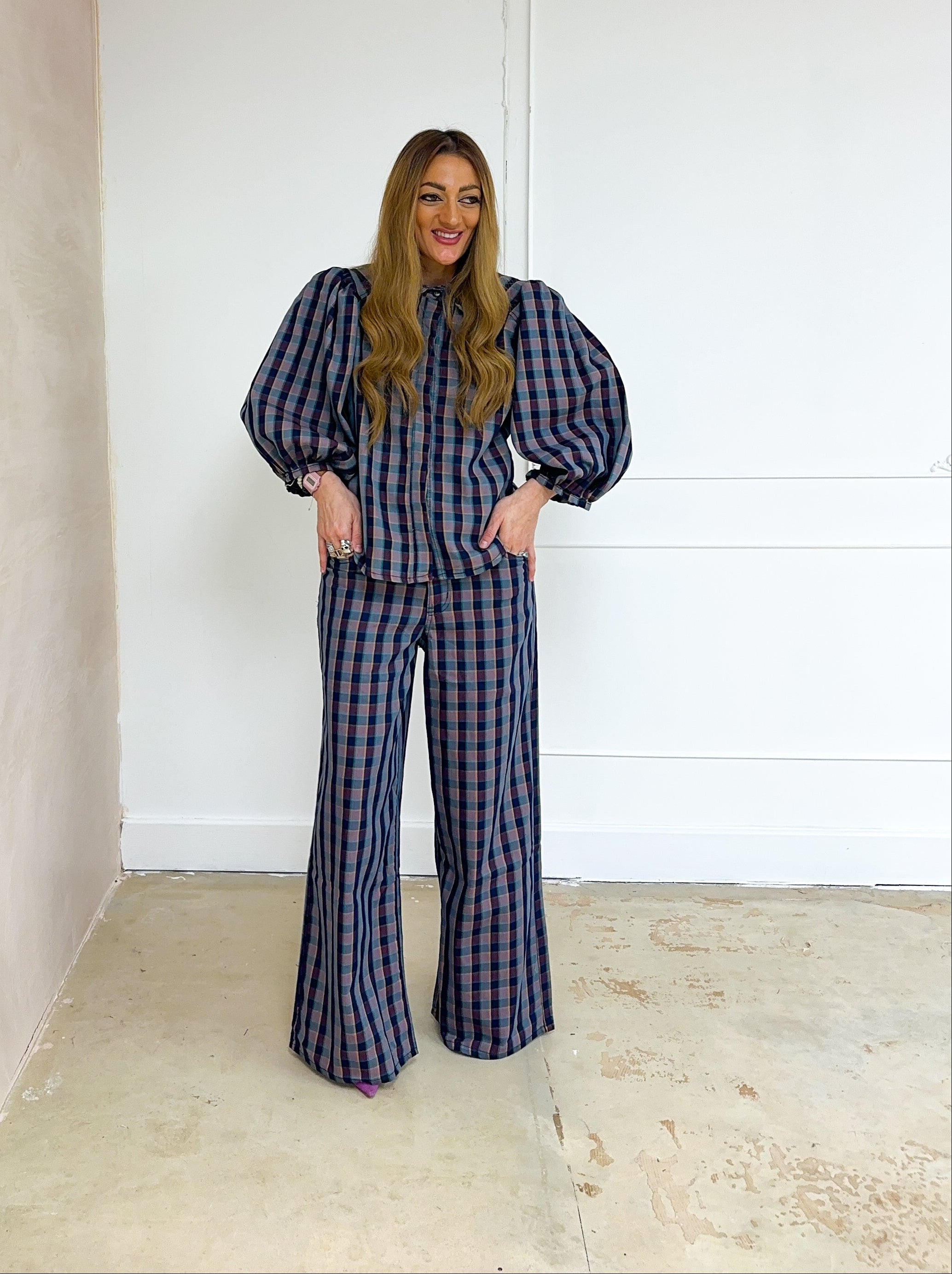 Woman wearing a plaid outfit standing in a minimalistic room with white walls and a gray ceiling.