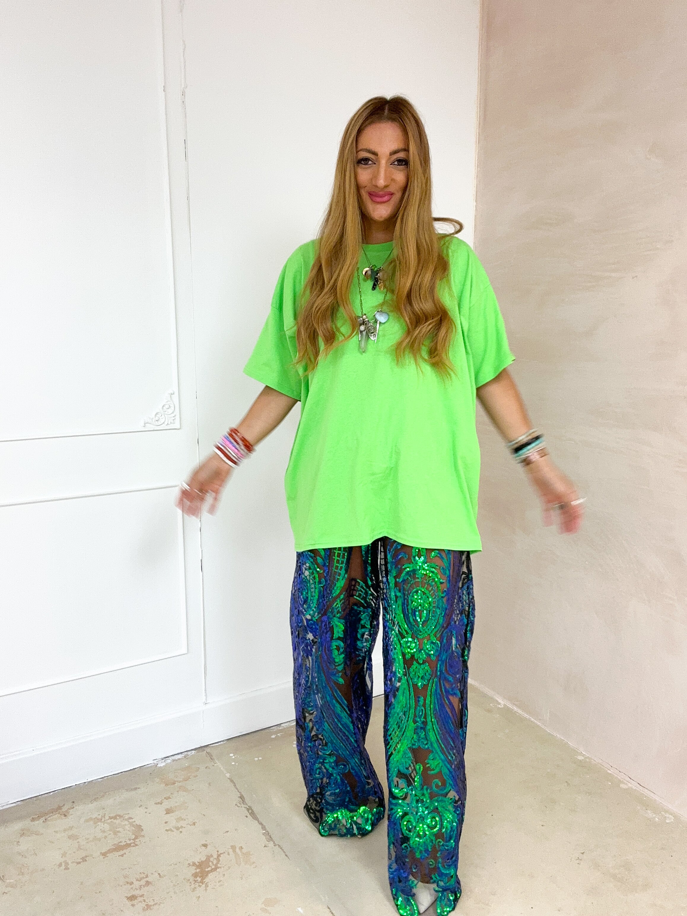 Woman wearing a bright green top and patterned pants in a minimal indoor setting