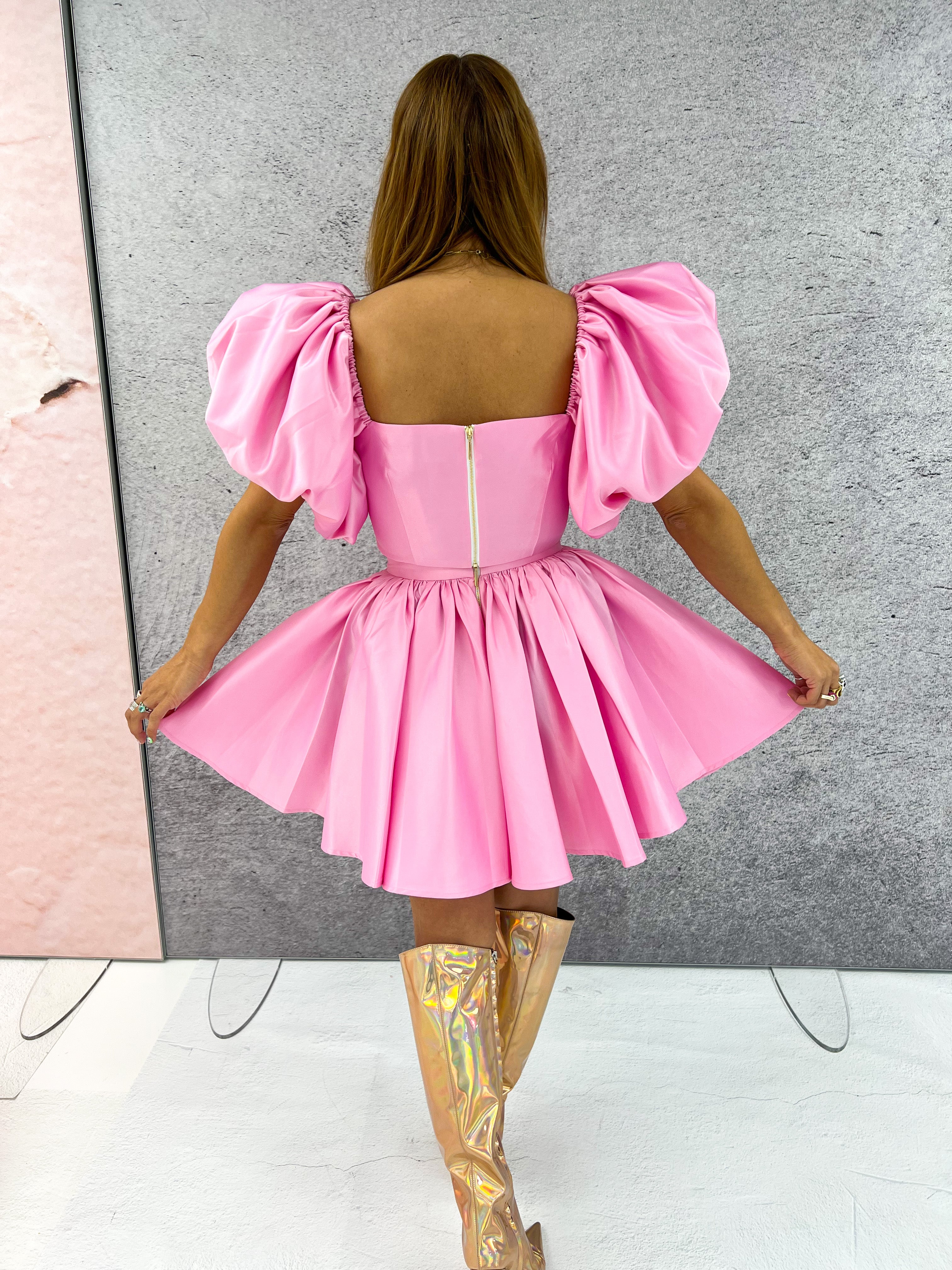 back of a model wearing an off-the-shoulder pink top with puffed sleeve styled with a pink flared skirt