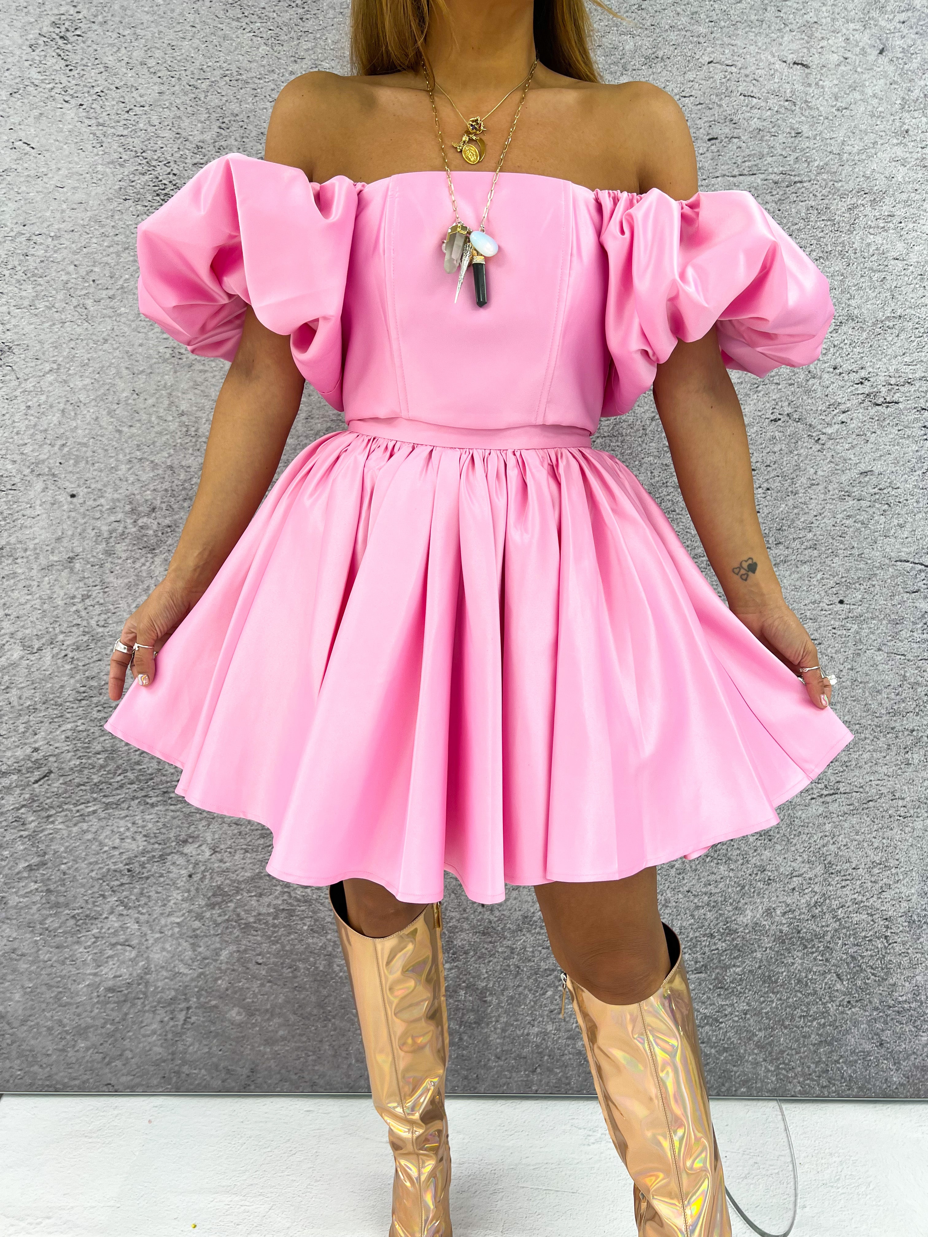 a model wearing an off-the-shoulder pink top with puffed sleeve styled with a pink flared skirt