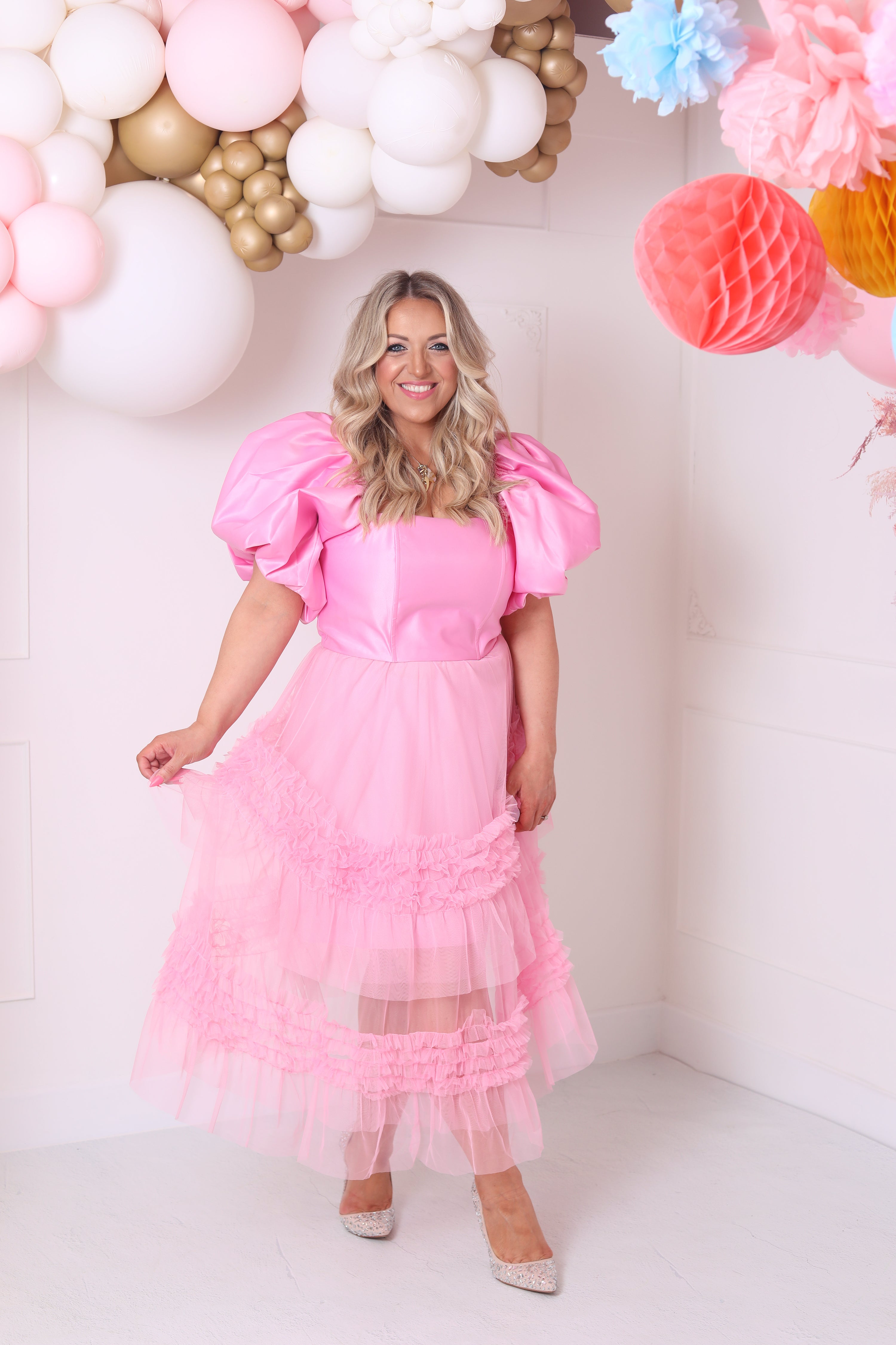 a model wearing an off-the-shoulder pink top with puffed sleeve styled with a pink tulle midi skirt