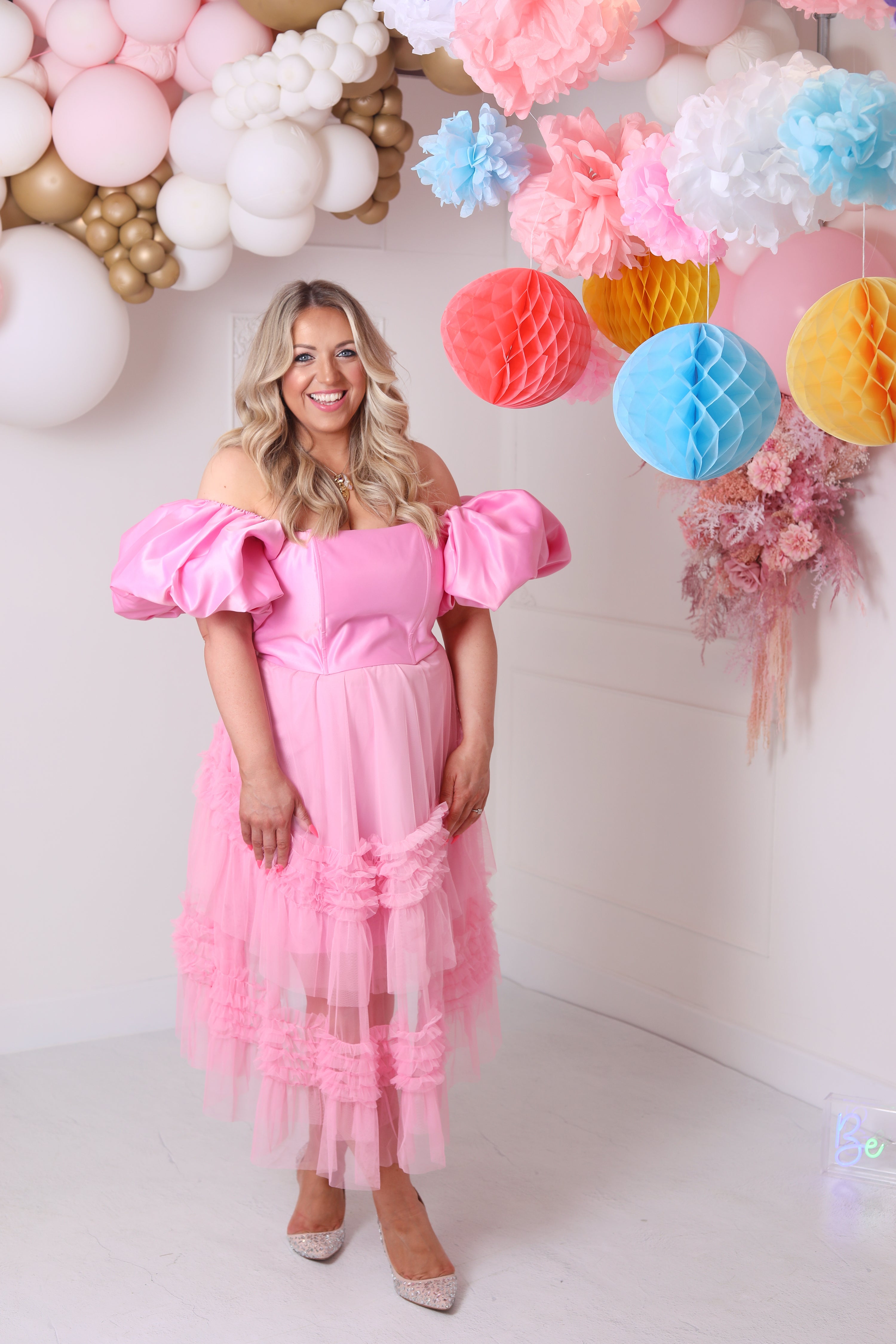 a model wearing an off-the-shoulder pink top with puffed sleeve styled with a pink tulle midi skirt