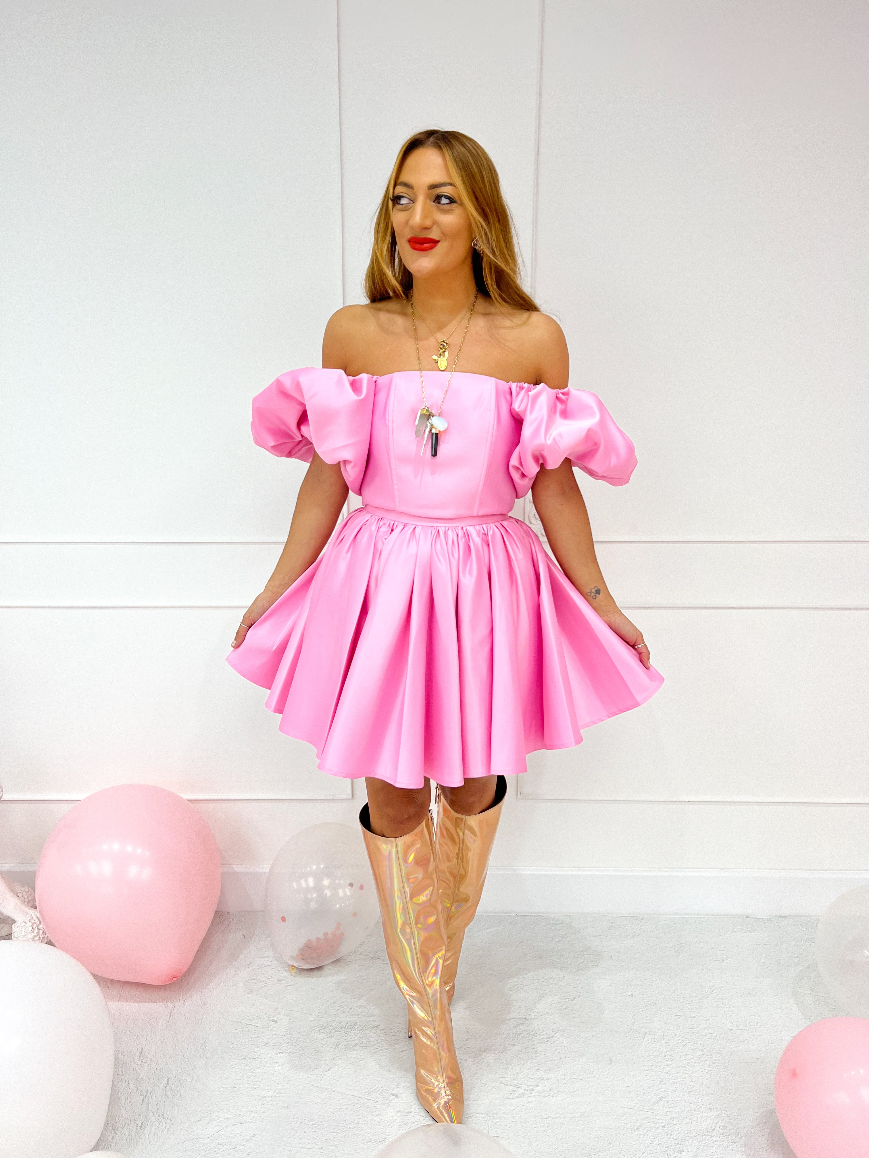 a model wearing an off-the-shoulder pink top with puffed sleeve styled with a pink flared skirt