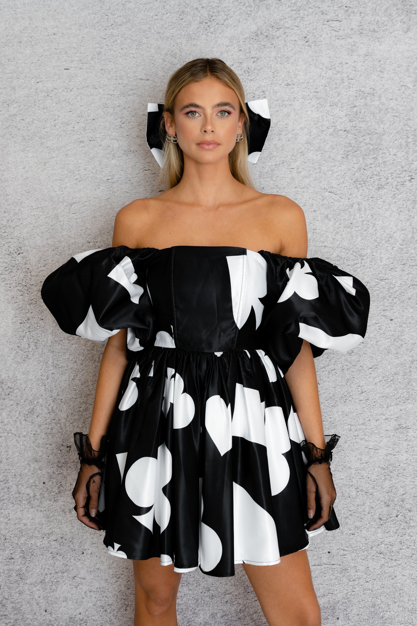 A women models a ace of spade printed off-the-shoulder dress featuring puff sleeves and a flared skirt.