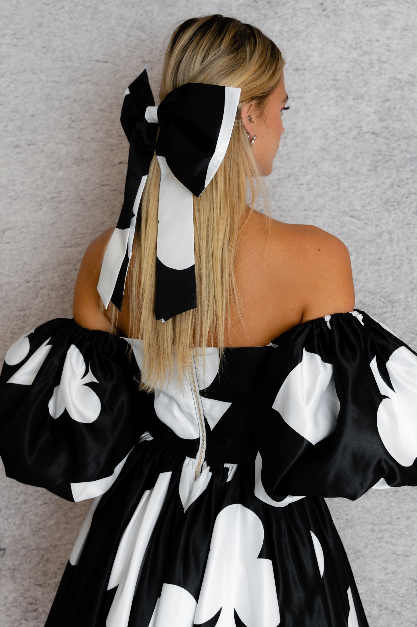 close up of a women models a ace of spade printed off-the-shoulder dress featuring puff sleeves and a flared skirt with a matching bow