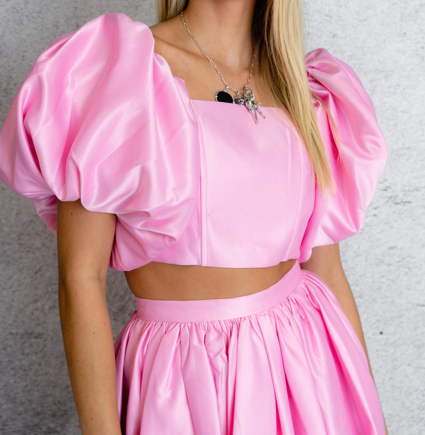 close up of a model wearing an off-the-shoulder pink top with puffed sleeve styled with a pink flared skirt