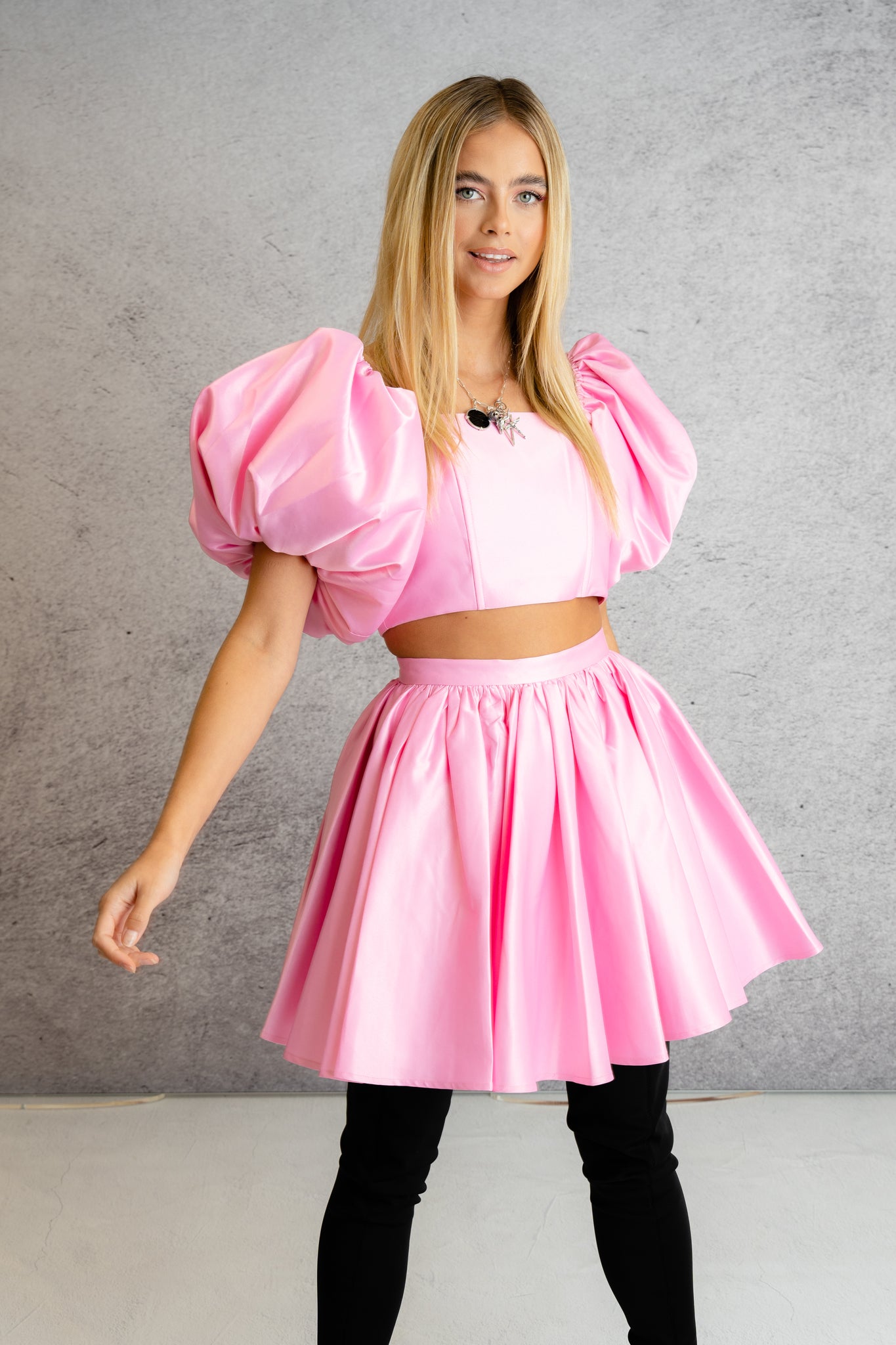 a model wearing an off-the-shoulder pink top with puffed sleeve styled with a pink flared skirt
