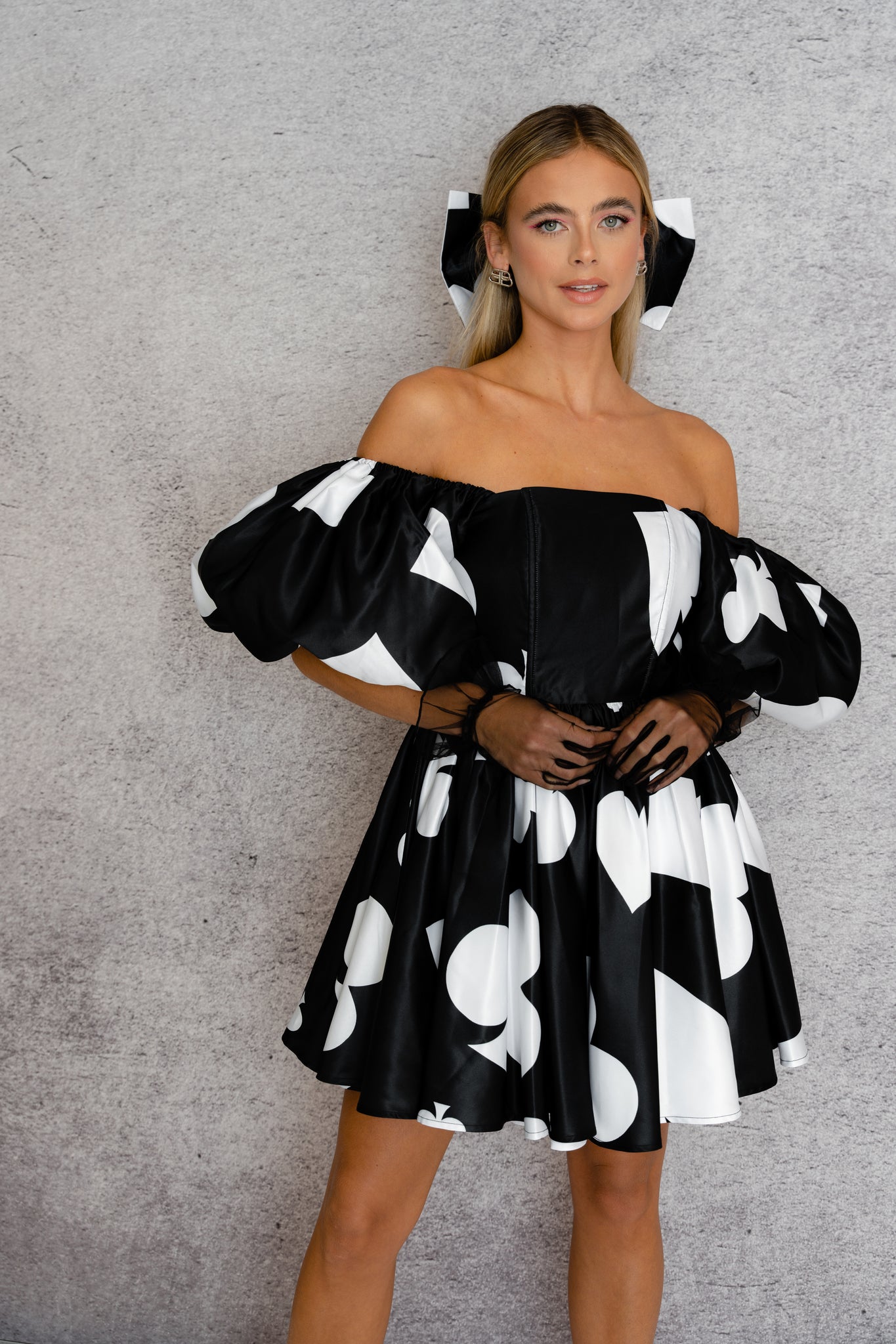 A women models a ace of spade printed off-the-shoulder dress featuring puff sleeves and a flared skirt.