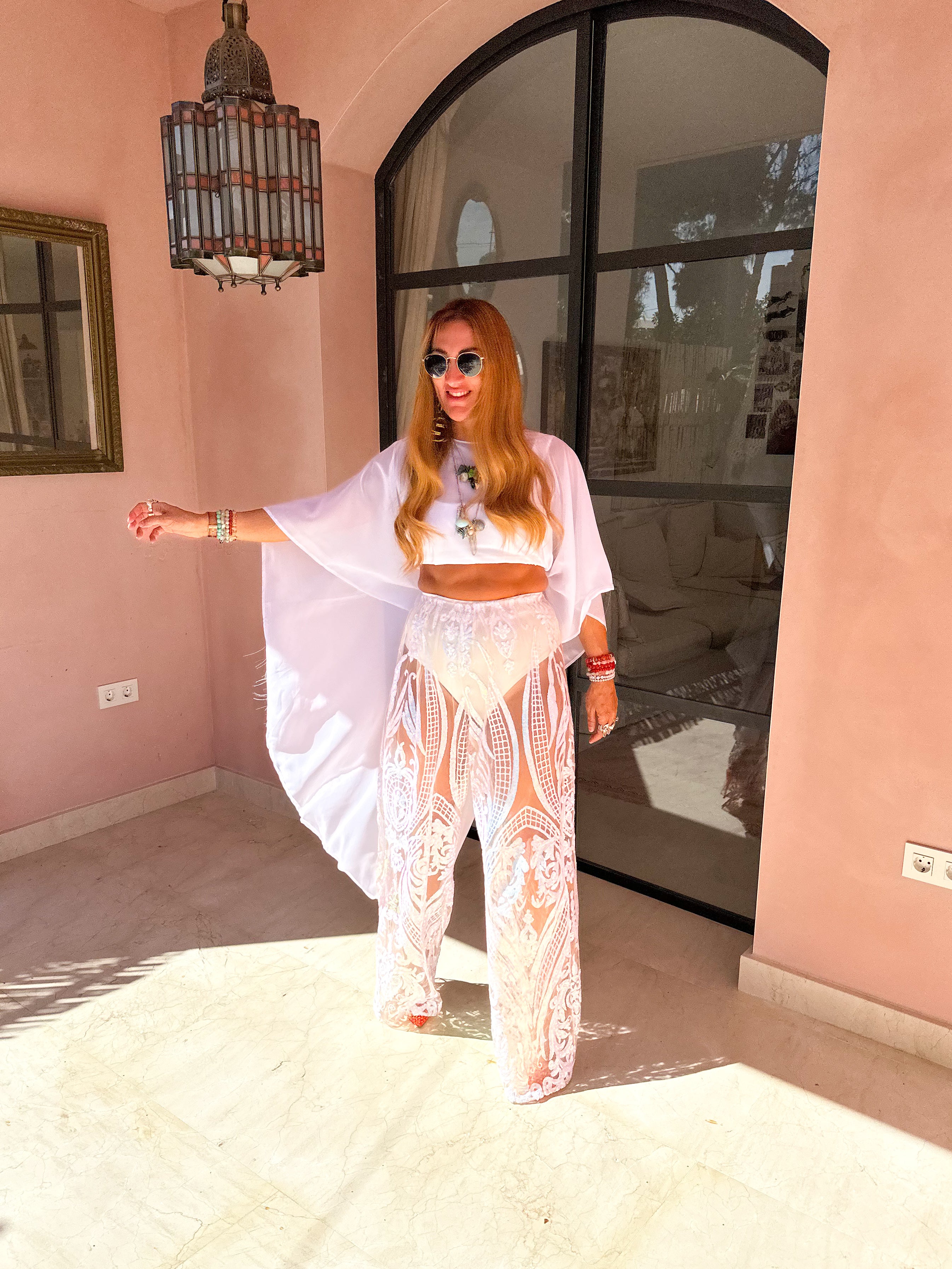 Woman in a white outfit standing in a room with pink walls and large windows.