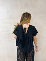 back of model wearing Embroidered Pleated Hem Swing style cropped Top In Black with t-shirt style sleeves styled with ballon lace trousers in black 