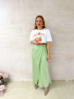  model wearing a white t-shirt with sliced orange graphics styled with satin wrap skirt in sage