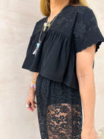 close up of model wearing Embroidered Pleated Hem Swing style cropped Top In Black with t-shirt style sleeves styled with ballon lace trousers in black 