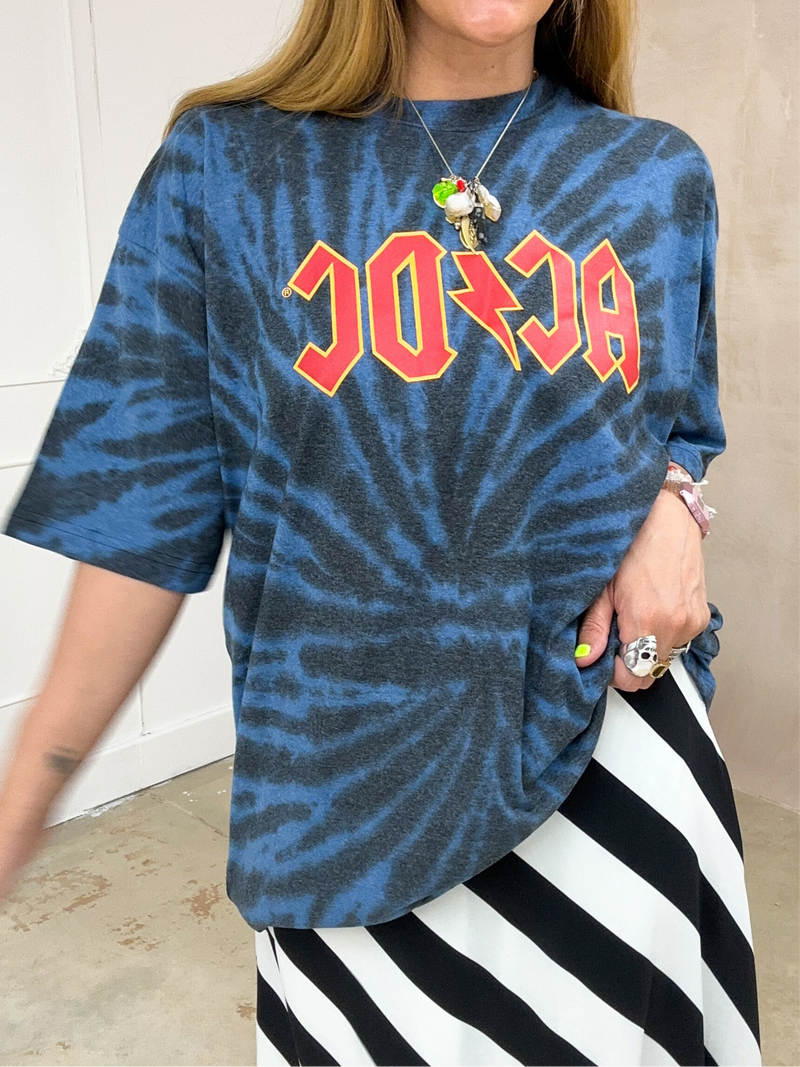 close up of a Model wearing a tie dye oversized graphic t-shirt featuring a AC/DC band logo, styled with a black and white horizontal stripe