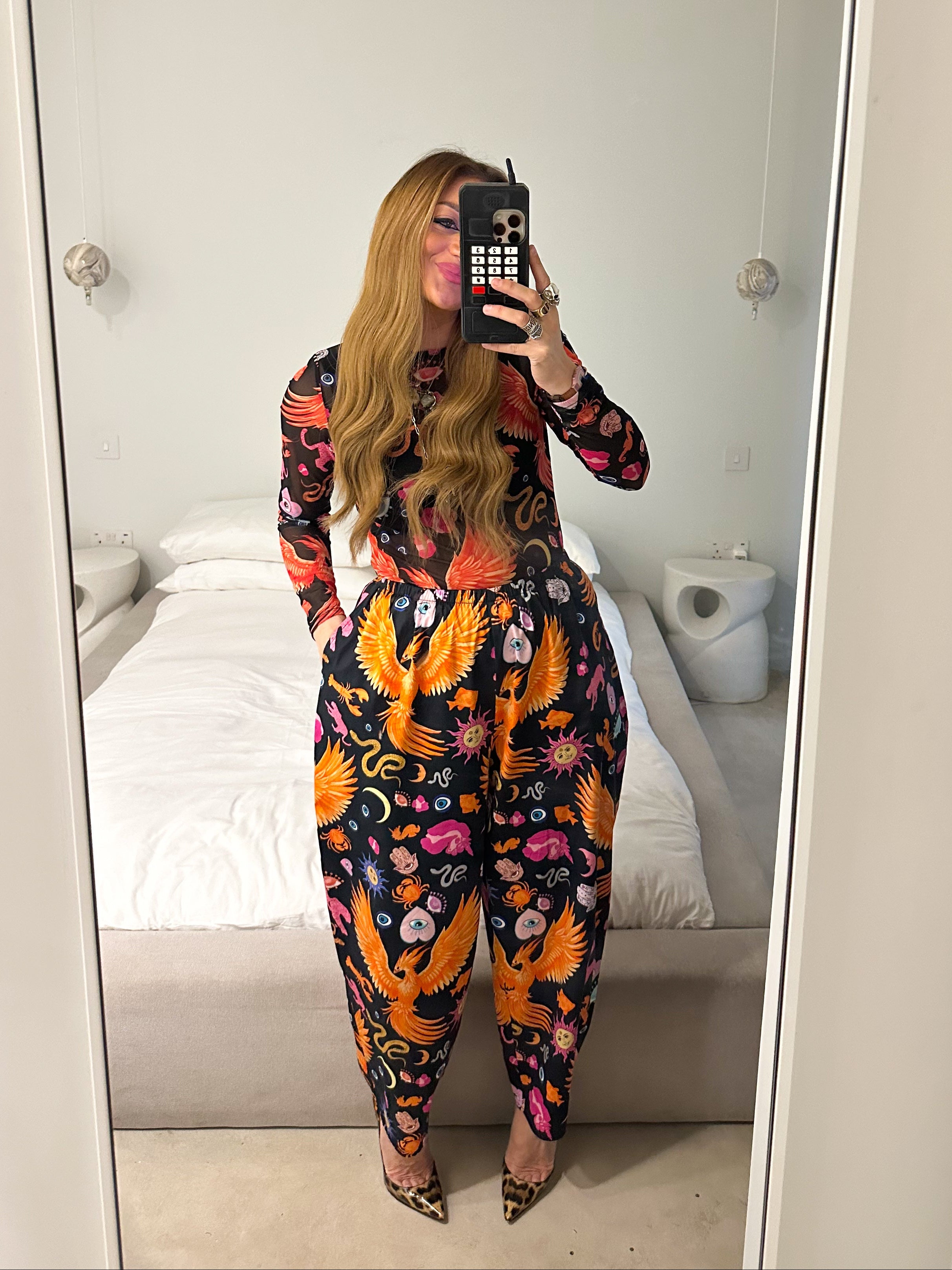 Person wearing a colorful outfit with floral and bird patterns in a room.