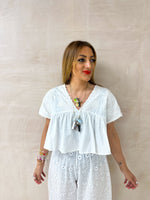 model wearing Embroidered Pleated Hem Swing style cropped Top In white with t-shirt style sleeves styled with Broderie Anglaise lace trousers in white