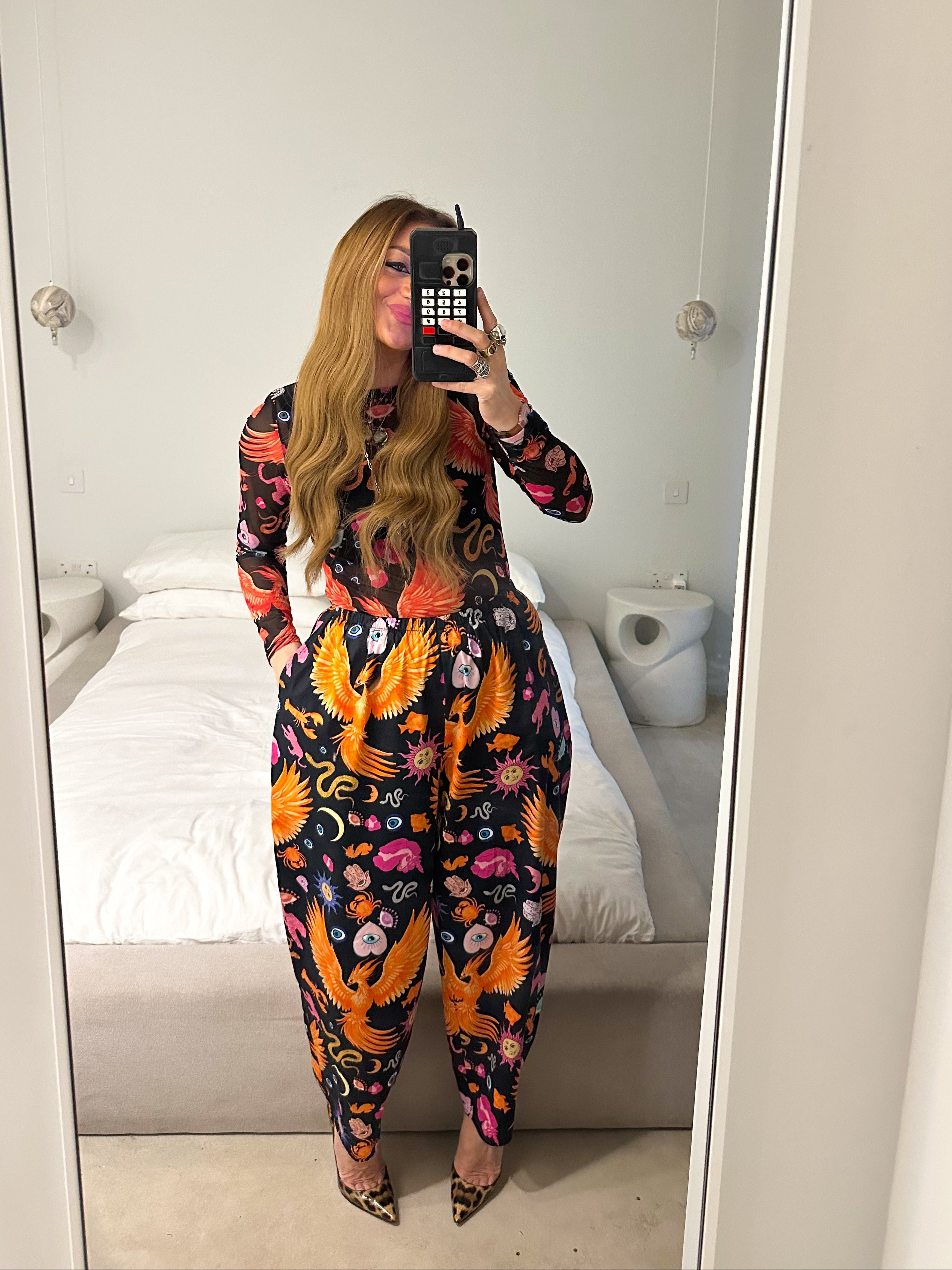 Person wearing a colorful outfit with floral and bird patterns in a room.