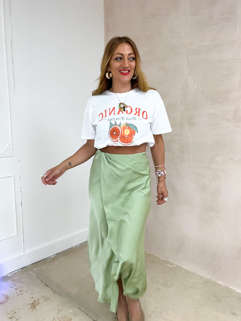  model wearing a white t-shirt with sliced orange graphics styled with satin wrap skirt in sage 