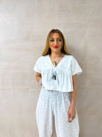 model wearing Embroidered Pleated Hem Swing style cropped Top In white with t-shirt style sleeves styled with Broderie Anglaise lace trousers in white