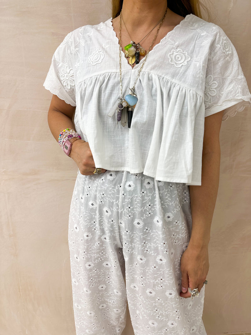 model wearing Embroidered Pleated Hem Swing style cropped Top In white with t-shirt style sleeves styled with Broderie Anglaise lace trousers in white