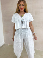 model wearing Embroidered Pleated Hem Swing style cropped Top In white with t-shirt style sleeves styled with Broderie Anglaise lace trousers in white